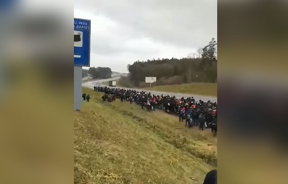 Setki migrantów na polsko-białoruskim przejściu granicznym. Towarzyszą im uzbrojeni ludzie w mundurach